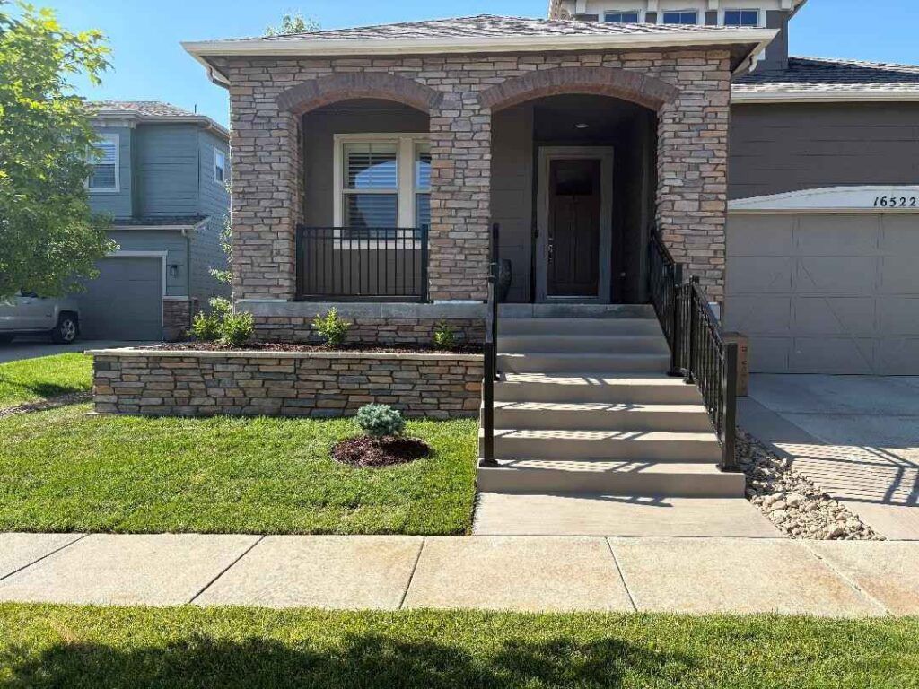 A stone-front porch with stairs leading to a front door, situated on a house with a lawn and driveway.