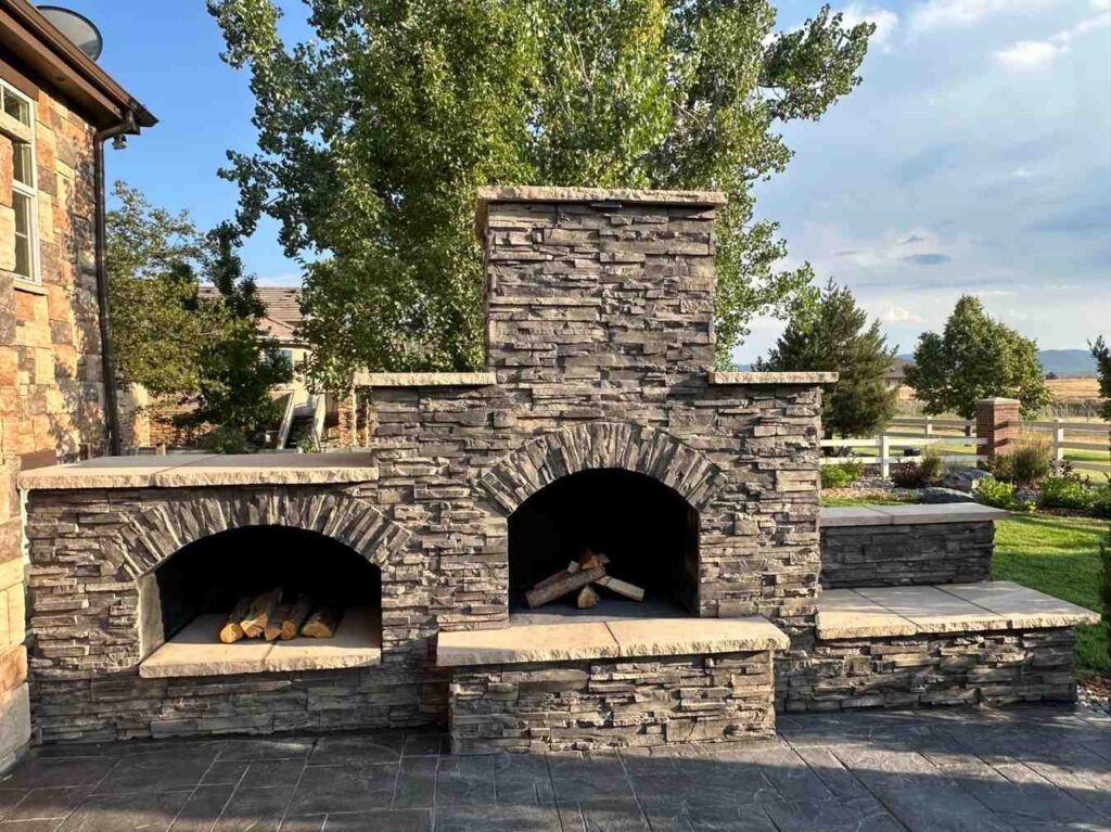 Outdoor stone fireplace and wood storage unit with a matching stone hearth and counter on a paved patio.