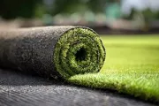 A rolled length of artificial green turf partially unrolled on a dark, textured surface.