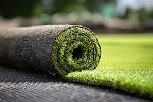 A rolled length of artificial green turf partially unrolled on a dark, textured surface.