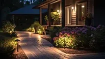 A stone path illuminated by small garden lights leads to a house porch surrounded by blooming hydrangeas at night.
