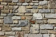 A rustic wall constructed from irregular, textured stones in shades of tan, gray, and brown.