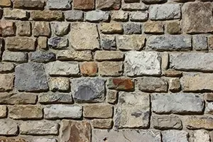 A rustic wall constructed from irregular, textured stones in shades of tan, gray, and brown.