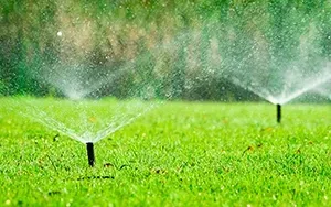 Two irrigation sprinklers spraying water over a vibrant green lawn.