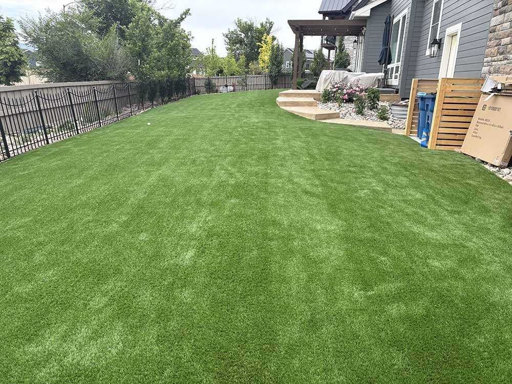 A wide, lush green lawn beside a house with a wooden patio and decorative metal fencing.