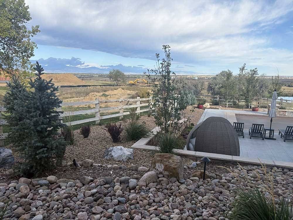 A landscaped yard with rock mulch, a white fence, and a patio area overlooking a distant, open desert landscape.