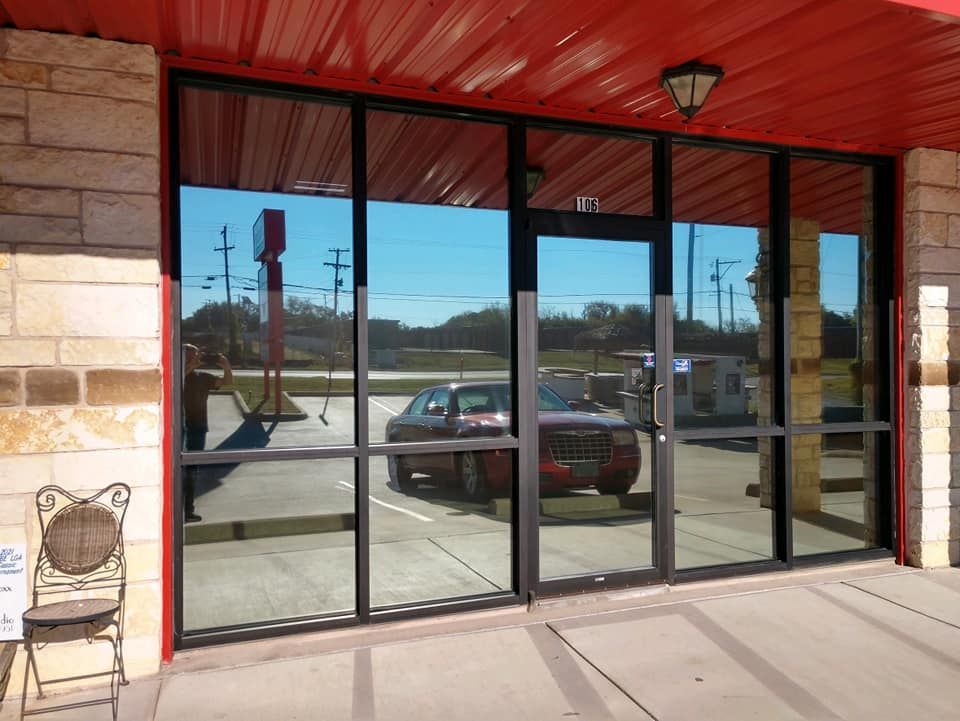 Exterior storefront with reflective windows; red awning, tan brick, and a car in the reflection.
