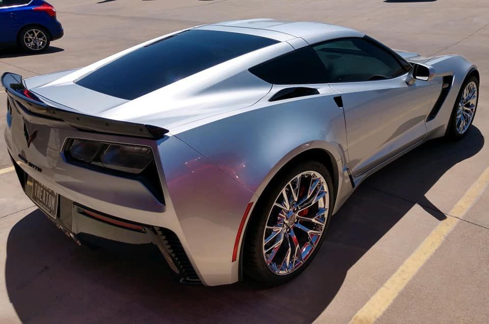 Silver Chevrolet Corvette sports car parked in a parking lot, sunlight reflecting off the body.