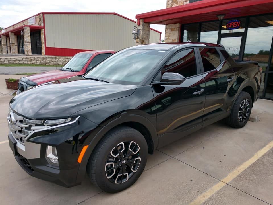 Black Hyundai Santa Cruz pickup truck parked outside a building with red trim.