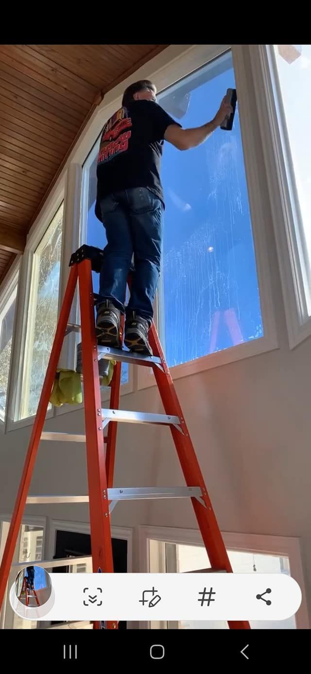 Person on a ladder, applying tint to a large window. Indoors, bright day, red ladder, blue sky.