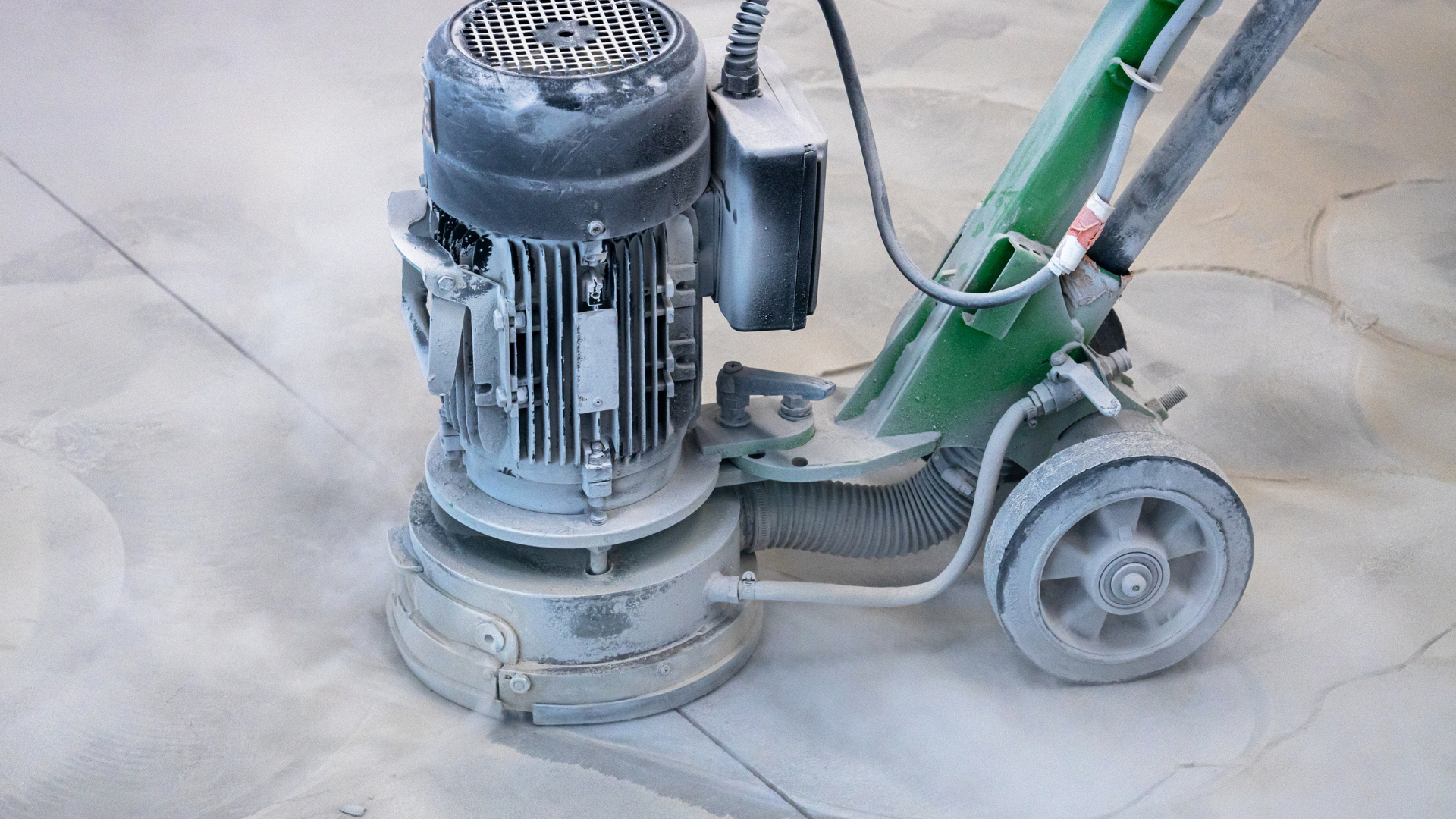 Concrete floor grinder sanding a dusty surface with a green handle and wheels