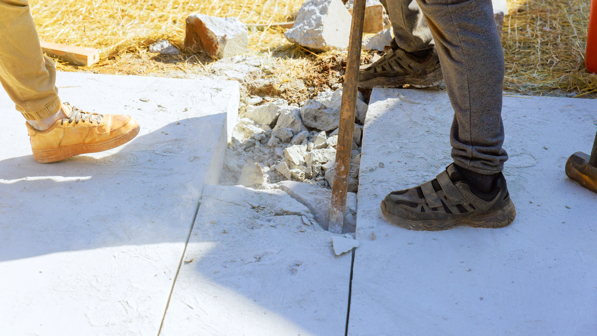 Workers using a jackhammer to break a white concrete slab outdoors