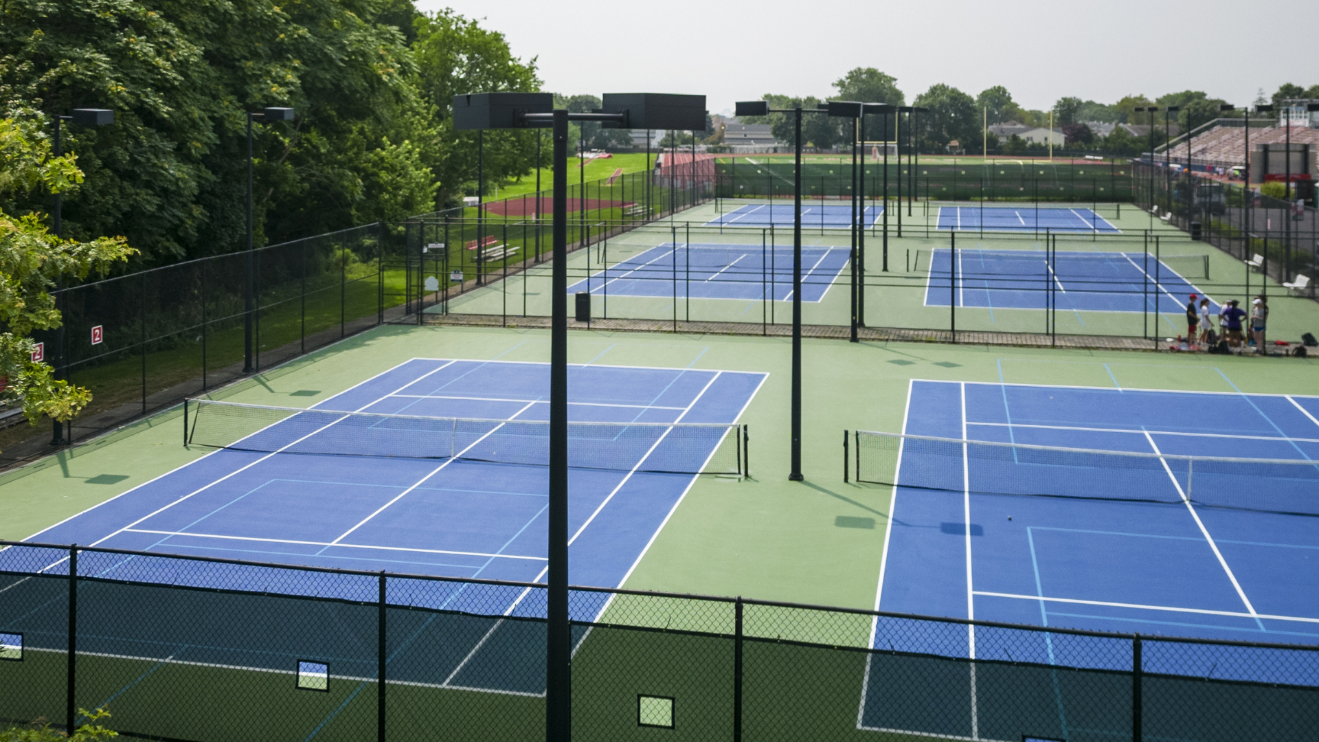 Multiple blue tennis courts with players on a sunny outdoor court complex
