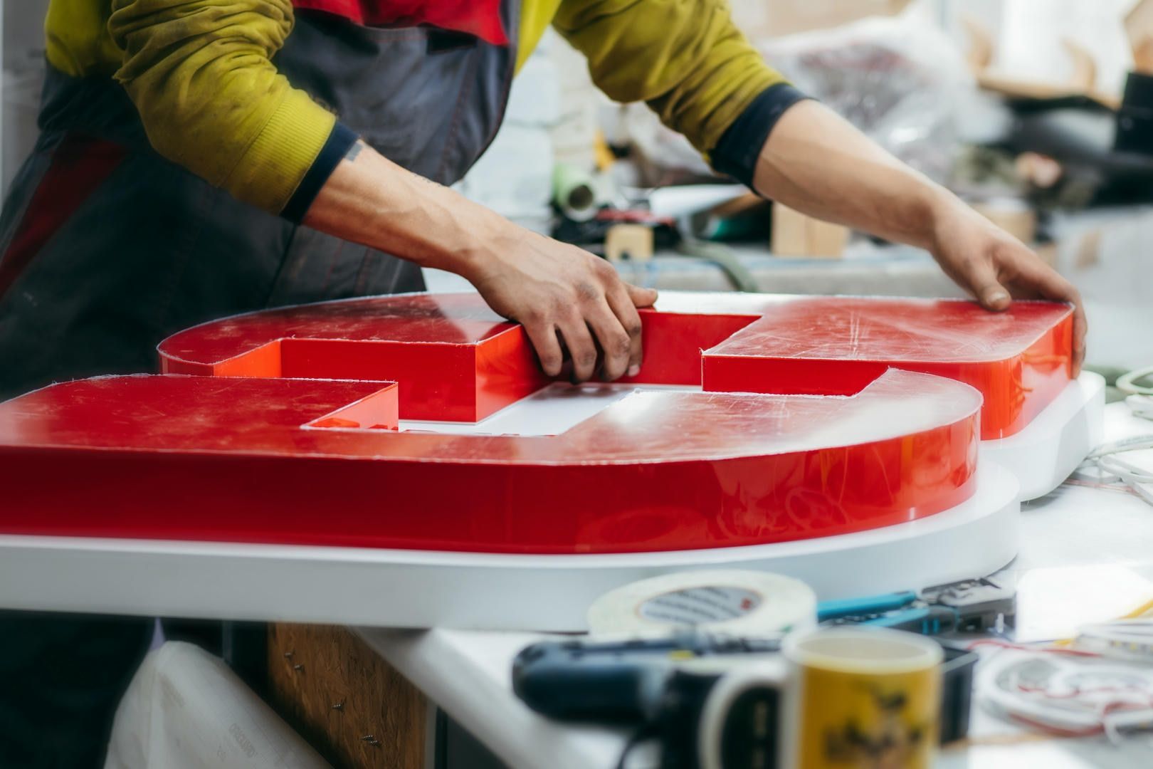 Person assembling a large, red, illuminated sign in a workshop.
