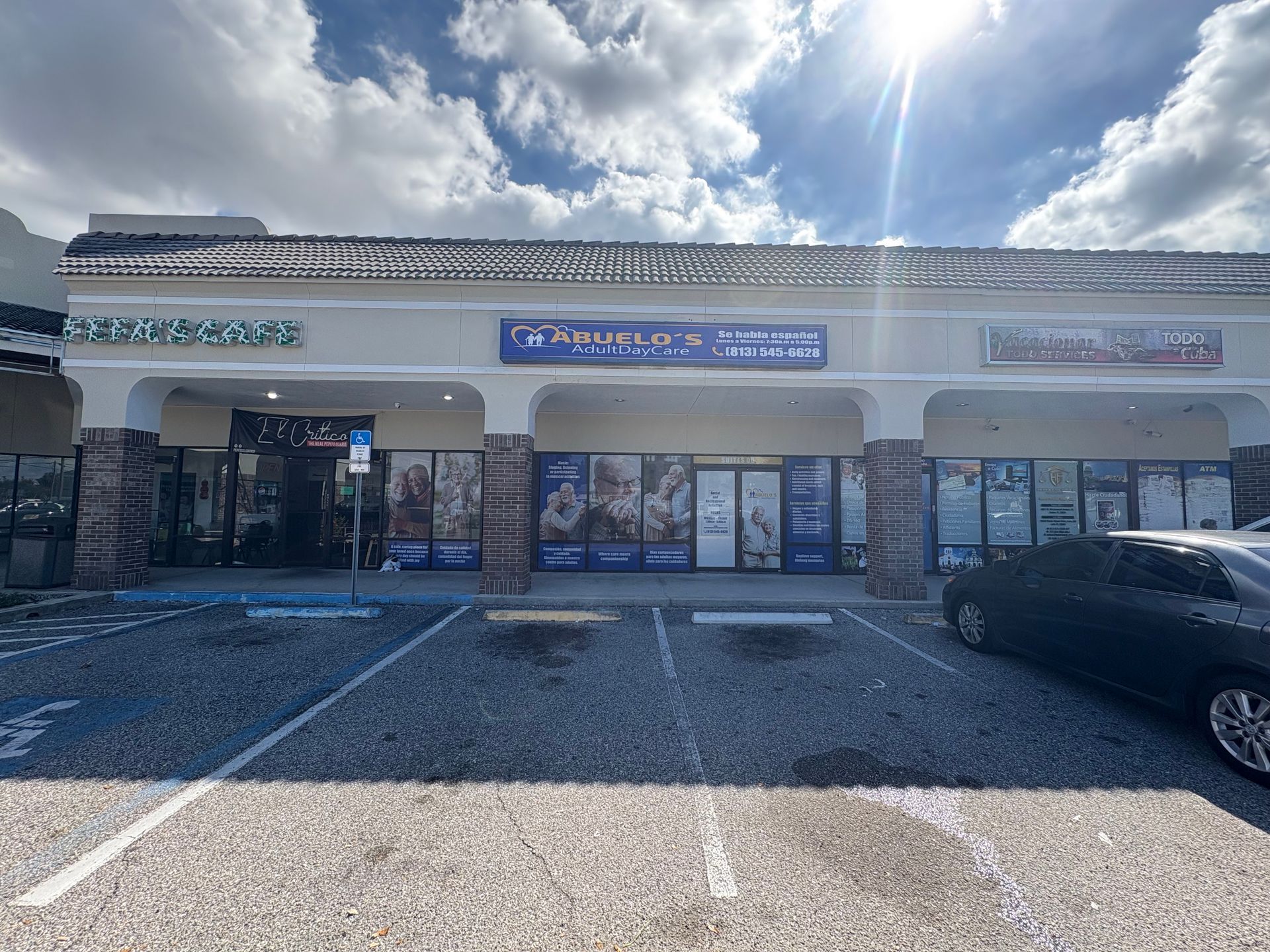 A strip mall on a sunny day with multiple storefronts and a parking lot. The middle store says 