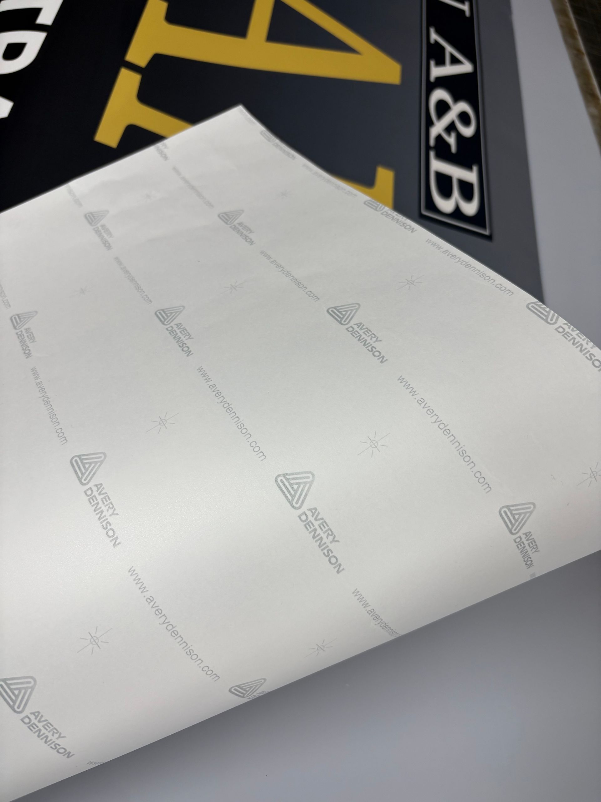 White paper with faint gray logos, partially covering a black and gold sign.