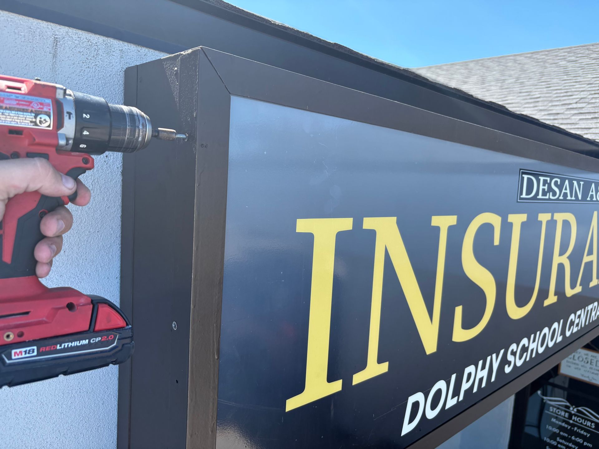 A person using a power drill to install a sign that reads 