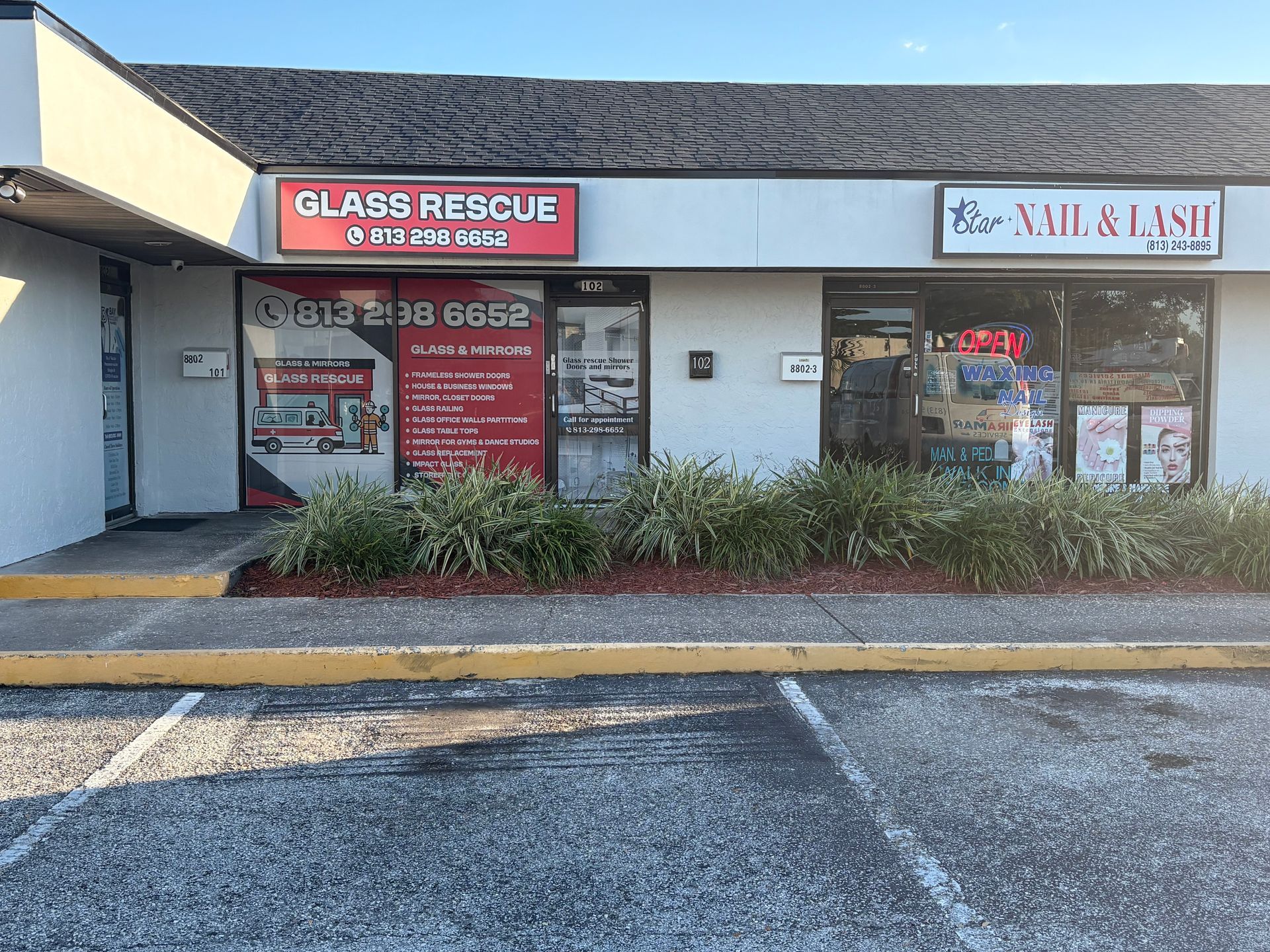 Exterior of a strip mall with a glass repair shop and a nail salon.