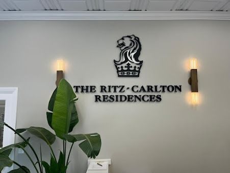 The Ritz-Carlton Residences logo on a beige wall, flanked by sconces and a plant.