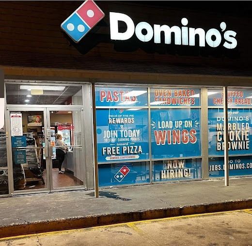 Domino's storefront with blue and white advertising. A person is inside near the entrance.