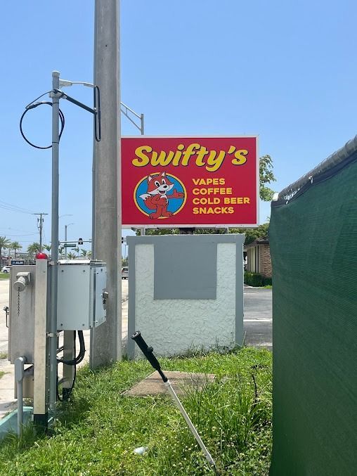 Sign for Swifty's, a store offering vapes, coffee, cold beer, and snacks, with a cartoon mascot on a red sign.