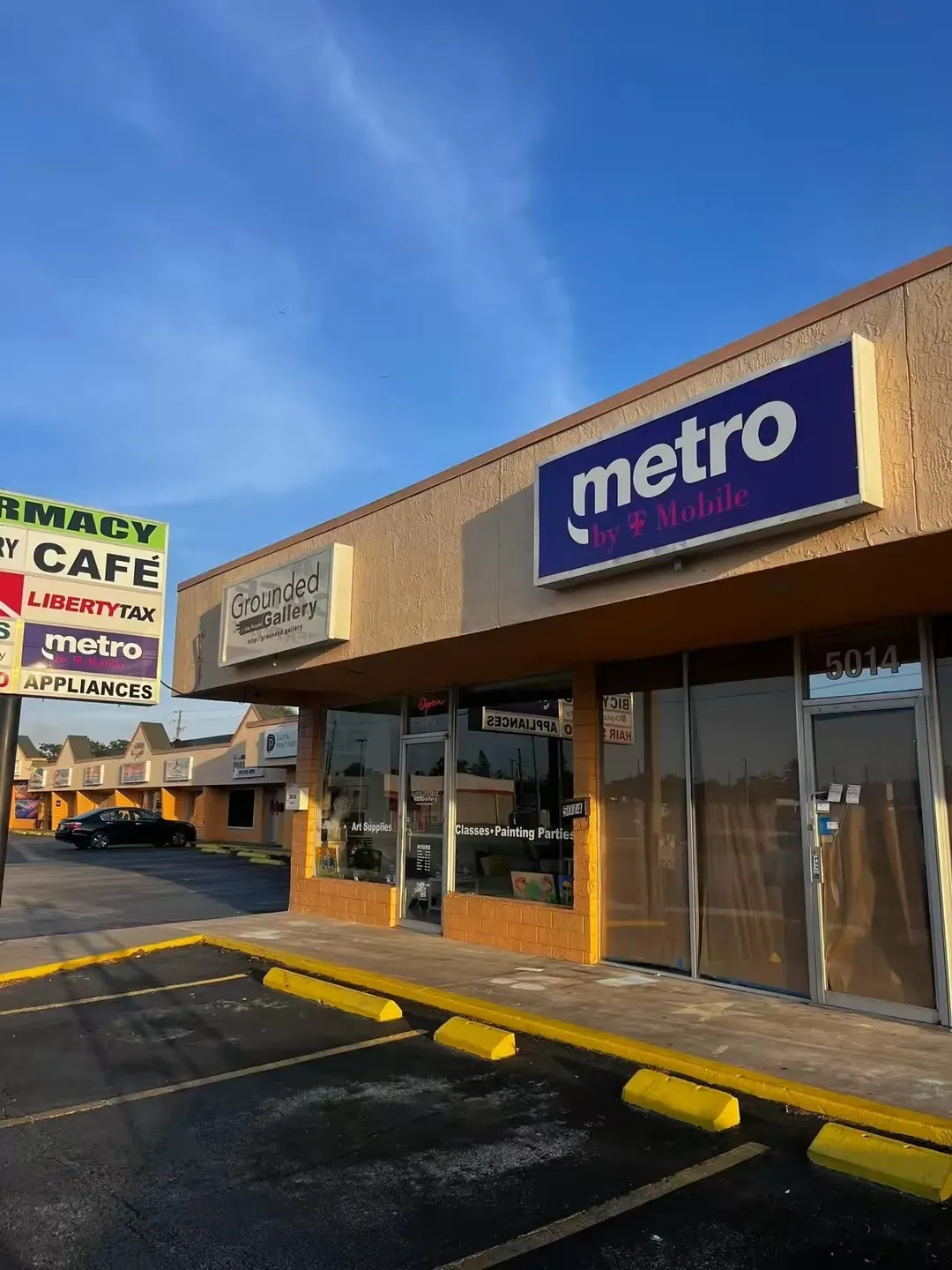 Exterior view of a strip mall with a Metro by T-Mobile store; blue sign, tan building, and parking lot.