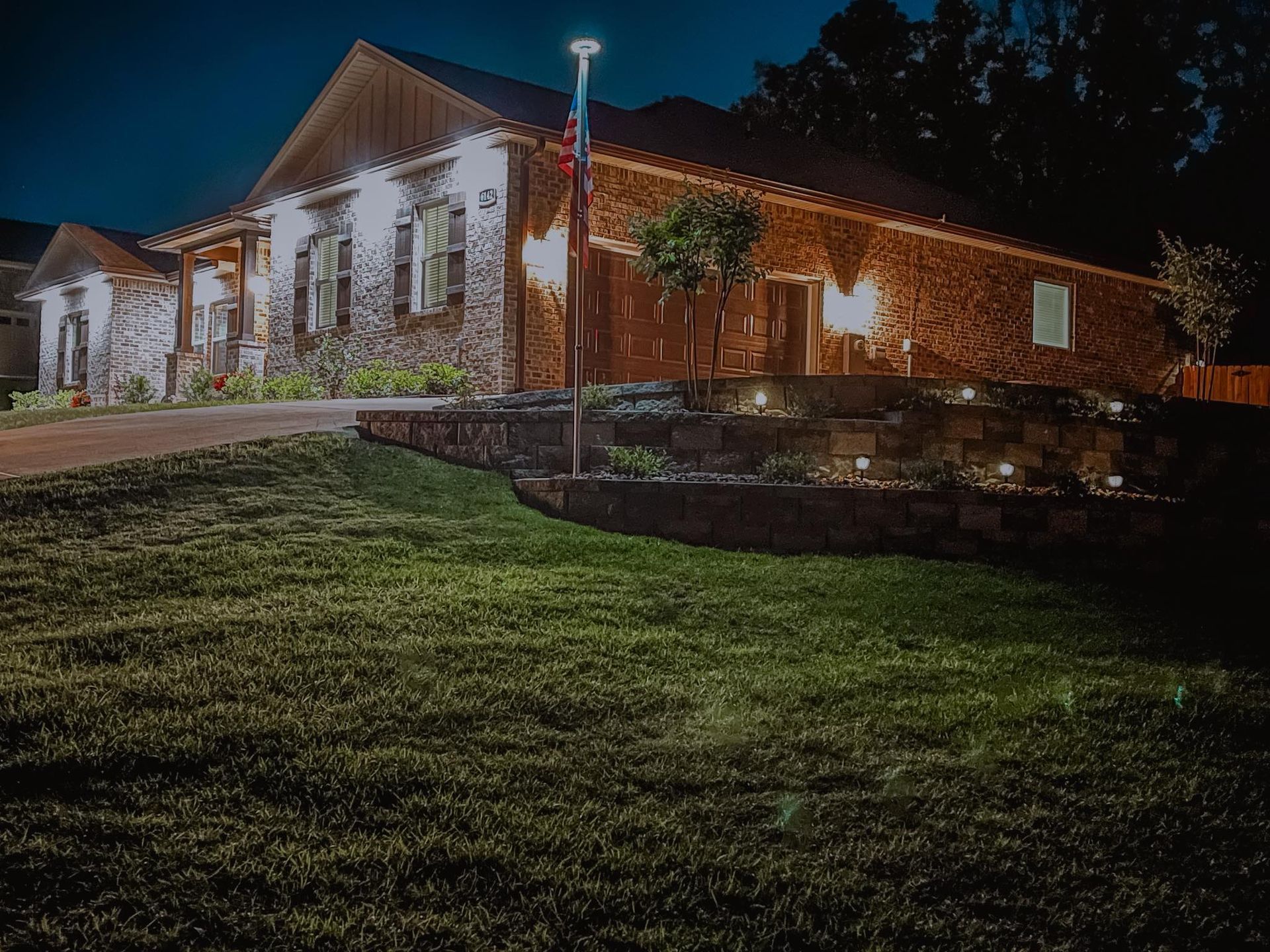 Stone building lit by warm string lights at night beside a grassy slope and stone wall