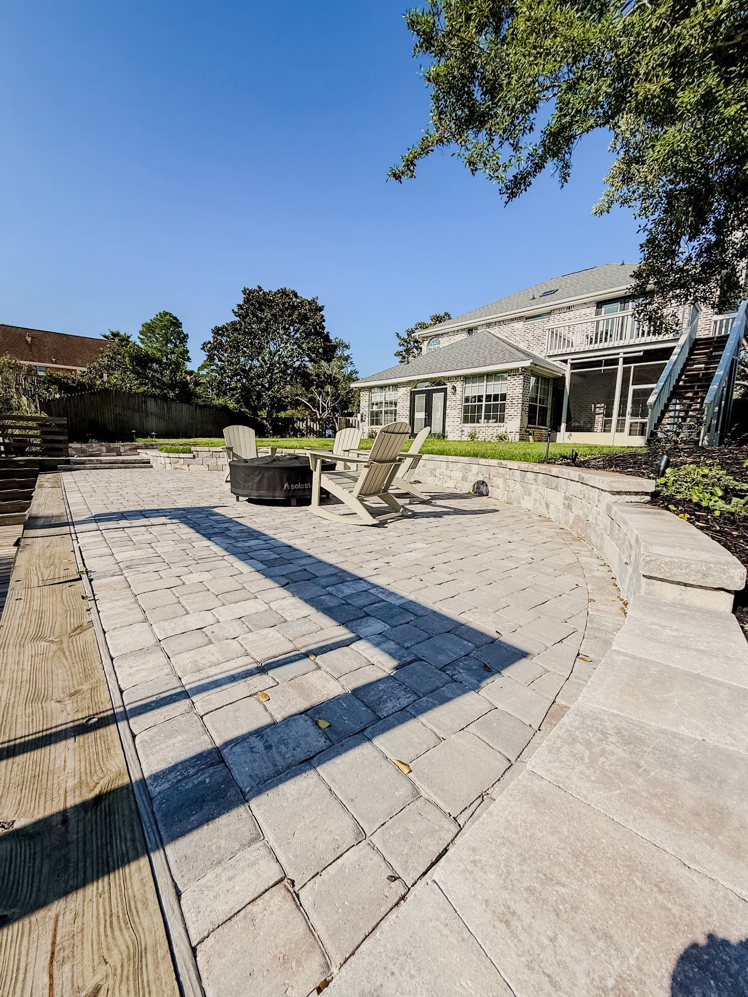 Sunny stone courtyard with trees, planters, and a modern building casting long shadows