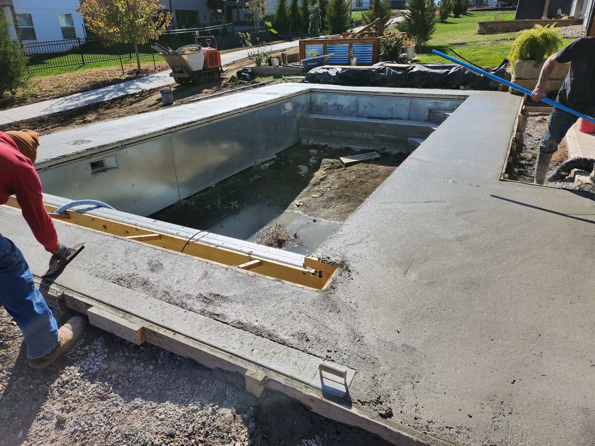 A man is laying concrete on top of a swimming pool.