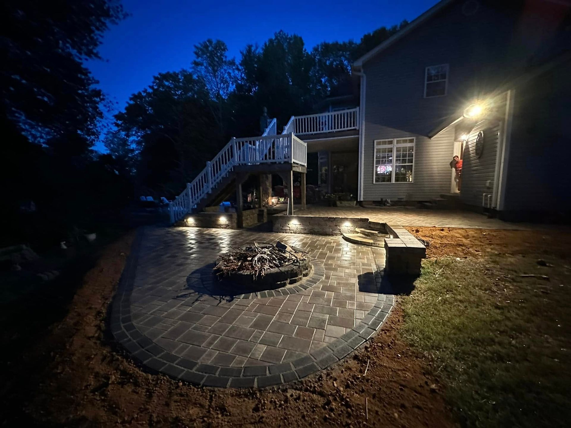 Night view of a backyard patio with a fire pit, lit steps, and a house.