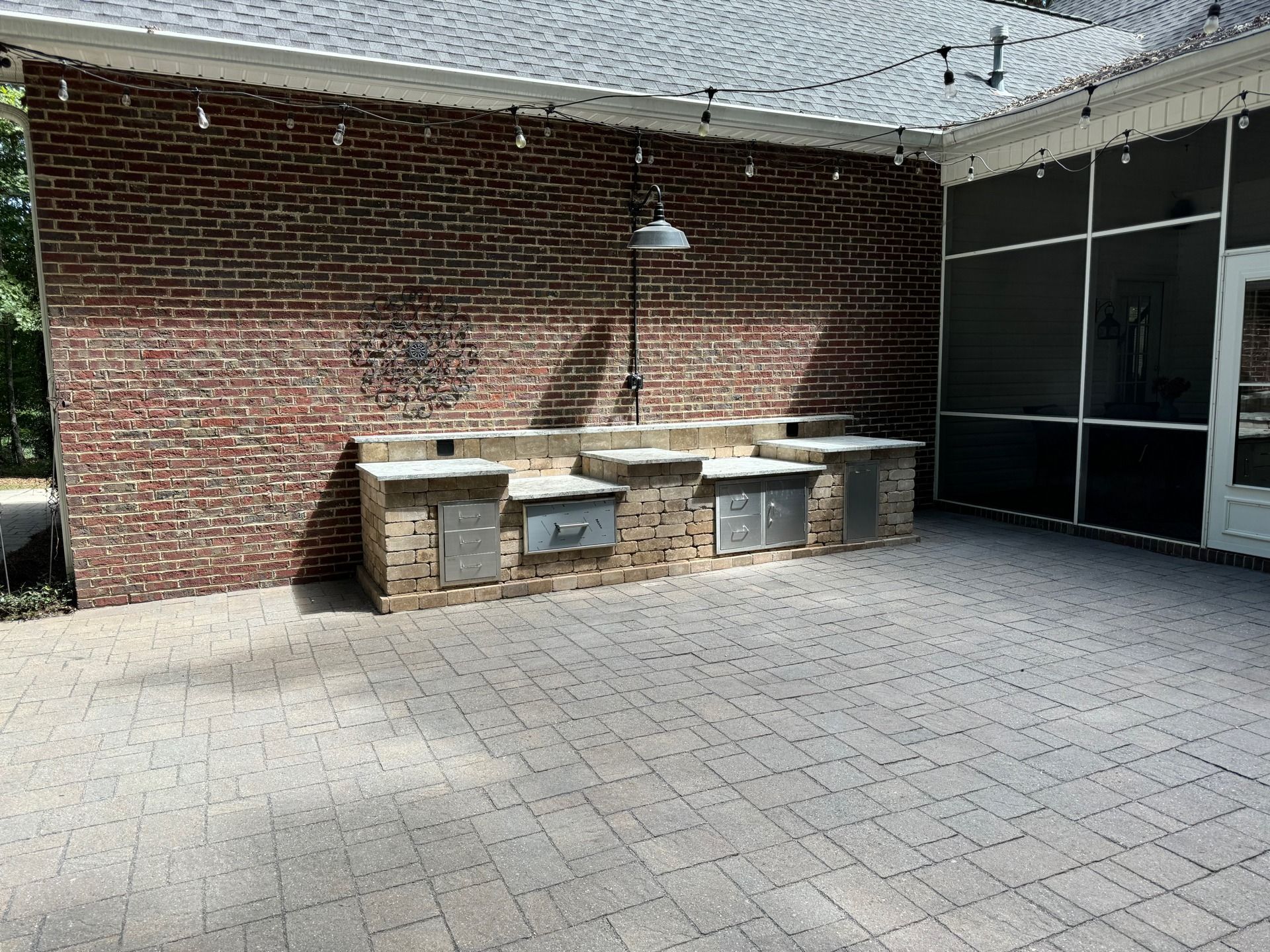 Outdoor kitchen with brick wall, stainless steel appliances, and a paved patio.
