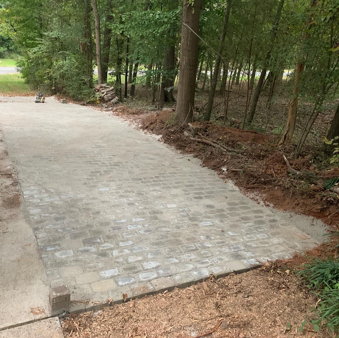 Paved driveway with a patterned gray surface leading into a wooded area.