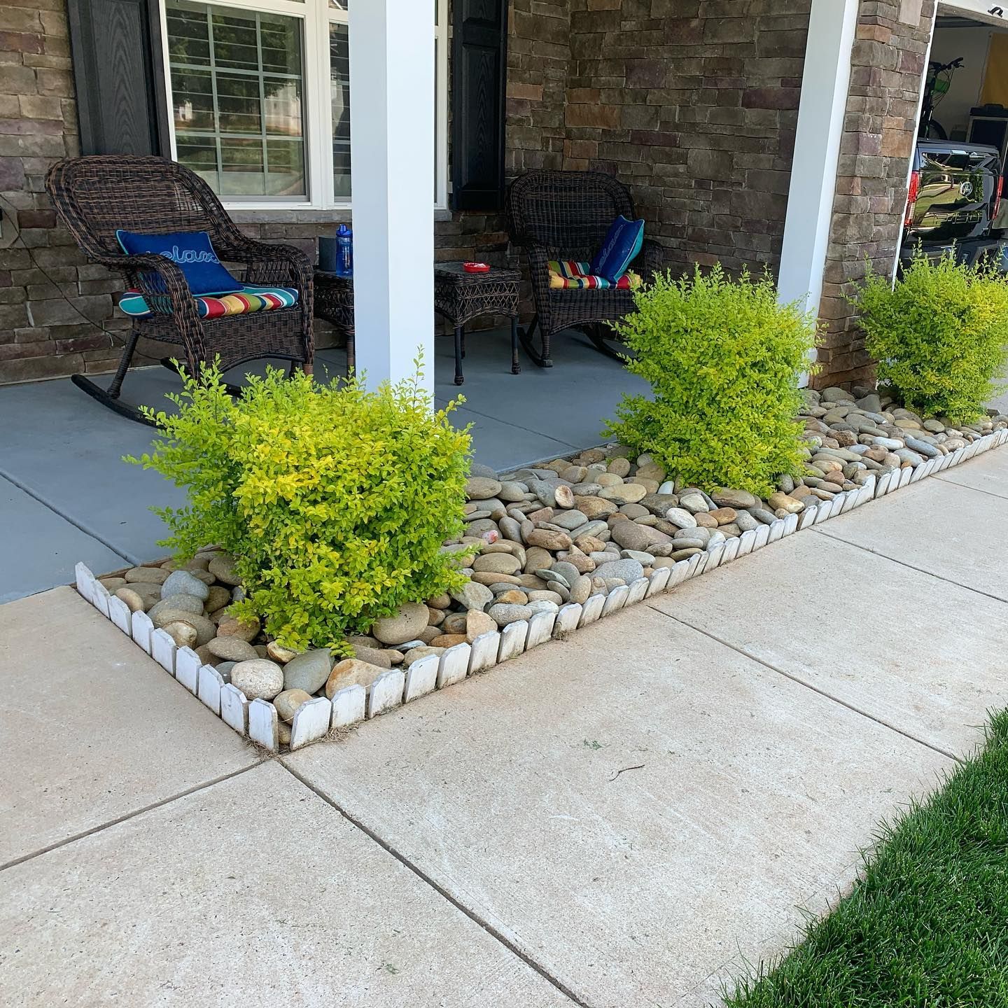 A porch with green shrubs, rocks, and a white-edged border next to a walkway.