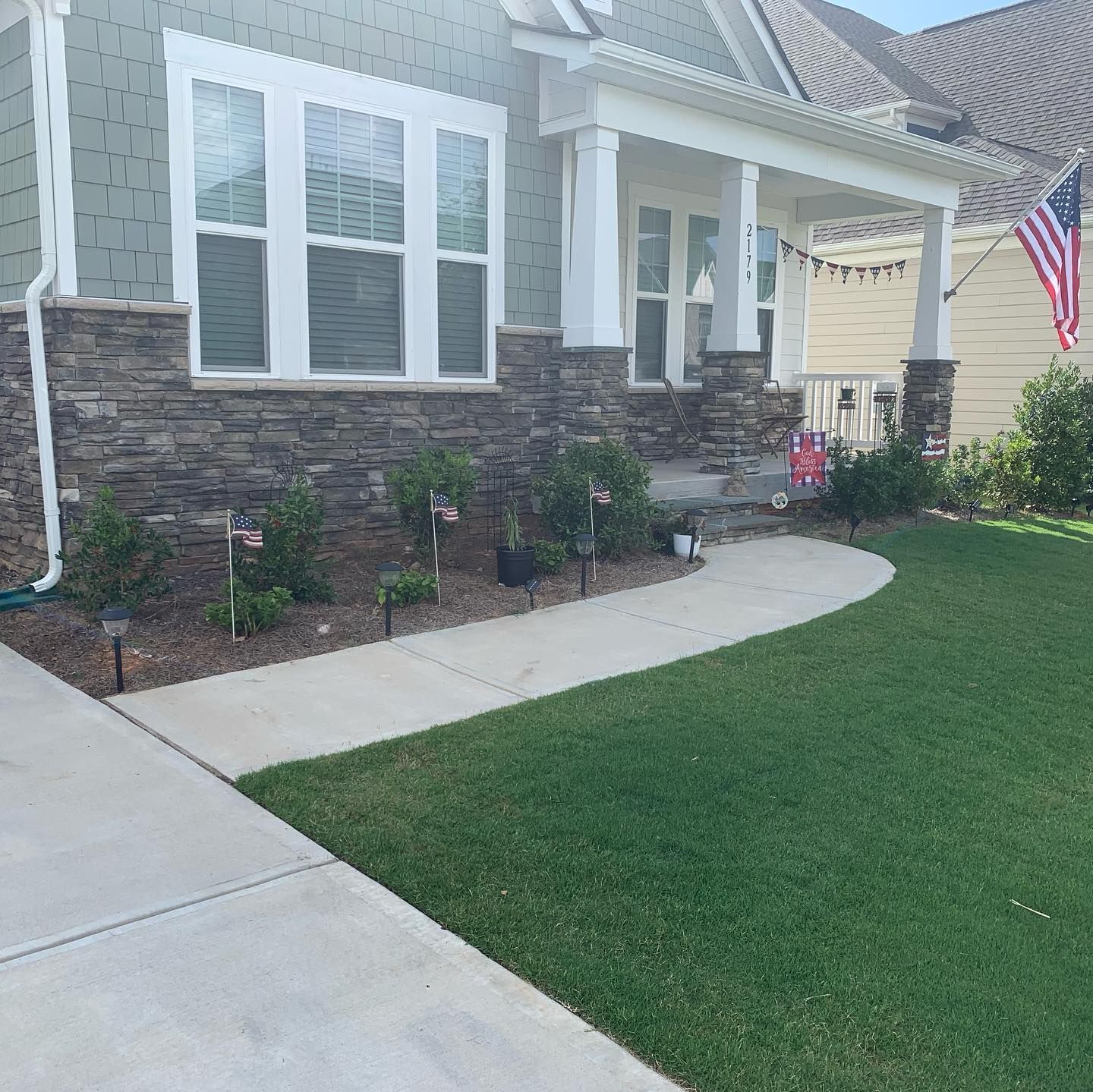 House front with stone accents, walkway, green lawn, and American flag.