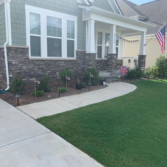 House front with stone accents, walkway, green lawn, and American flag.