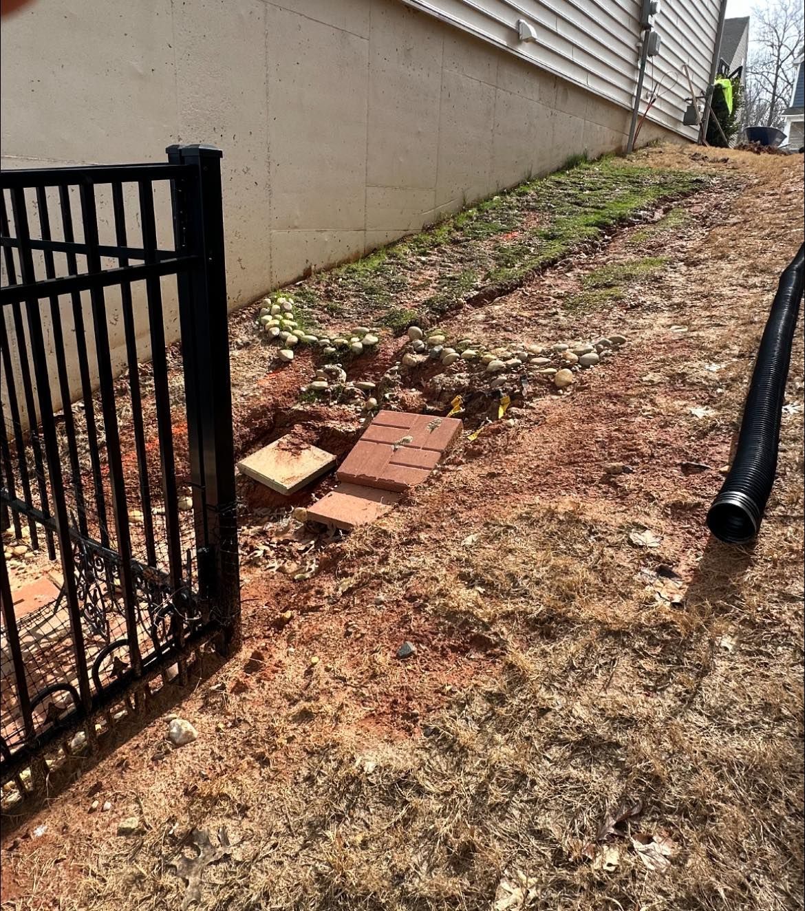 Black fence, open brick access to an underground structure in a yard next to a building.