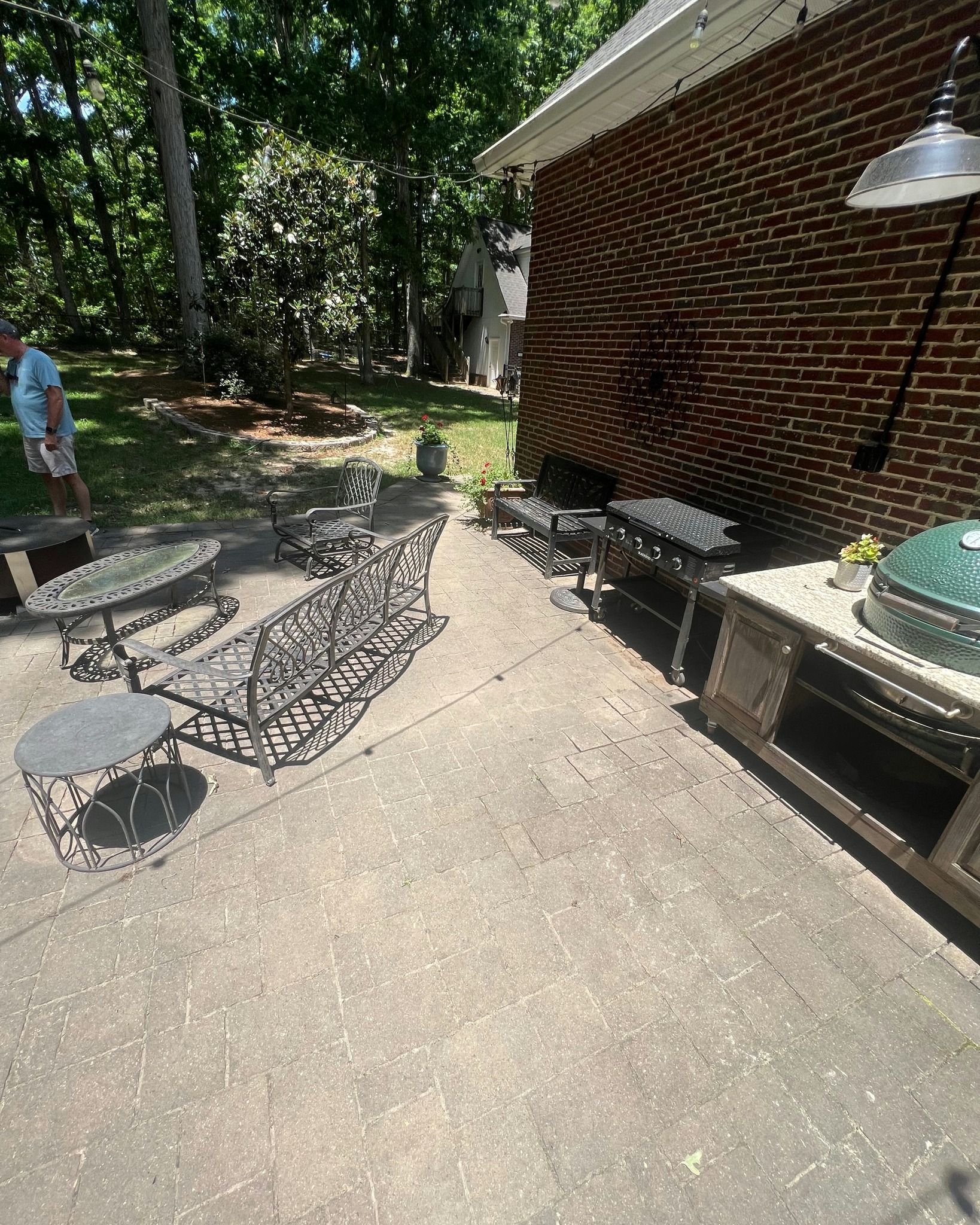 Outdoor patio with furniture, including a grill, tables, and a bench, next to a brick building.