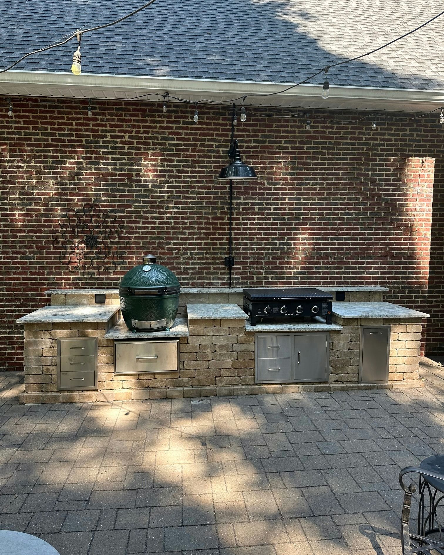 Outdoor kitchen with green Big Green Egg grill, built-in gas grill, brick wall background.
