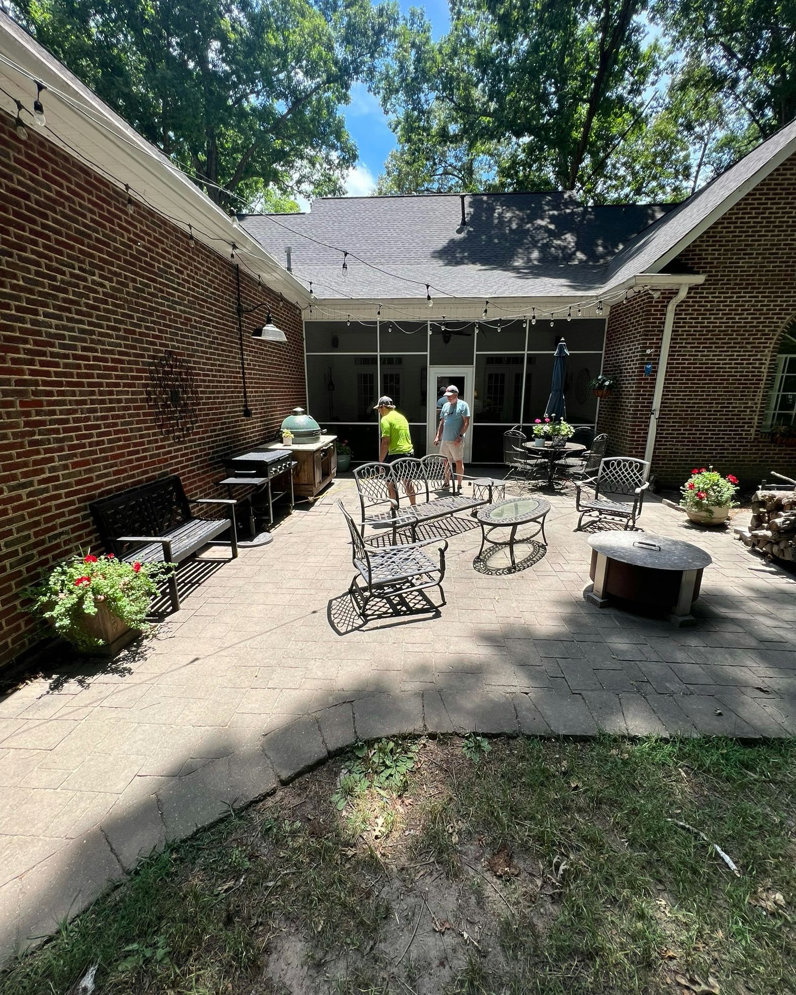 Brick patio with outdoor furniture, grill, and two people standing near a screened porch.