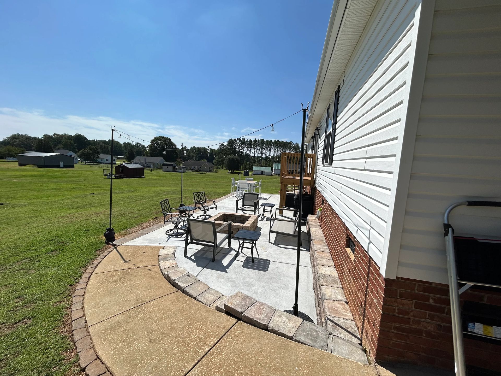 Patio with seating around a fire pit next to a house with a lawn and blue sky.