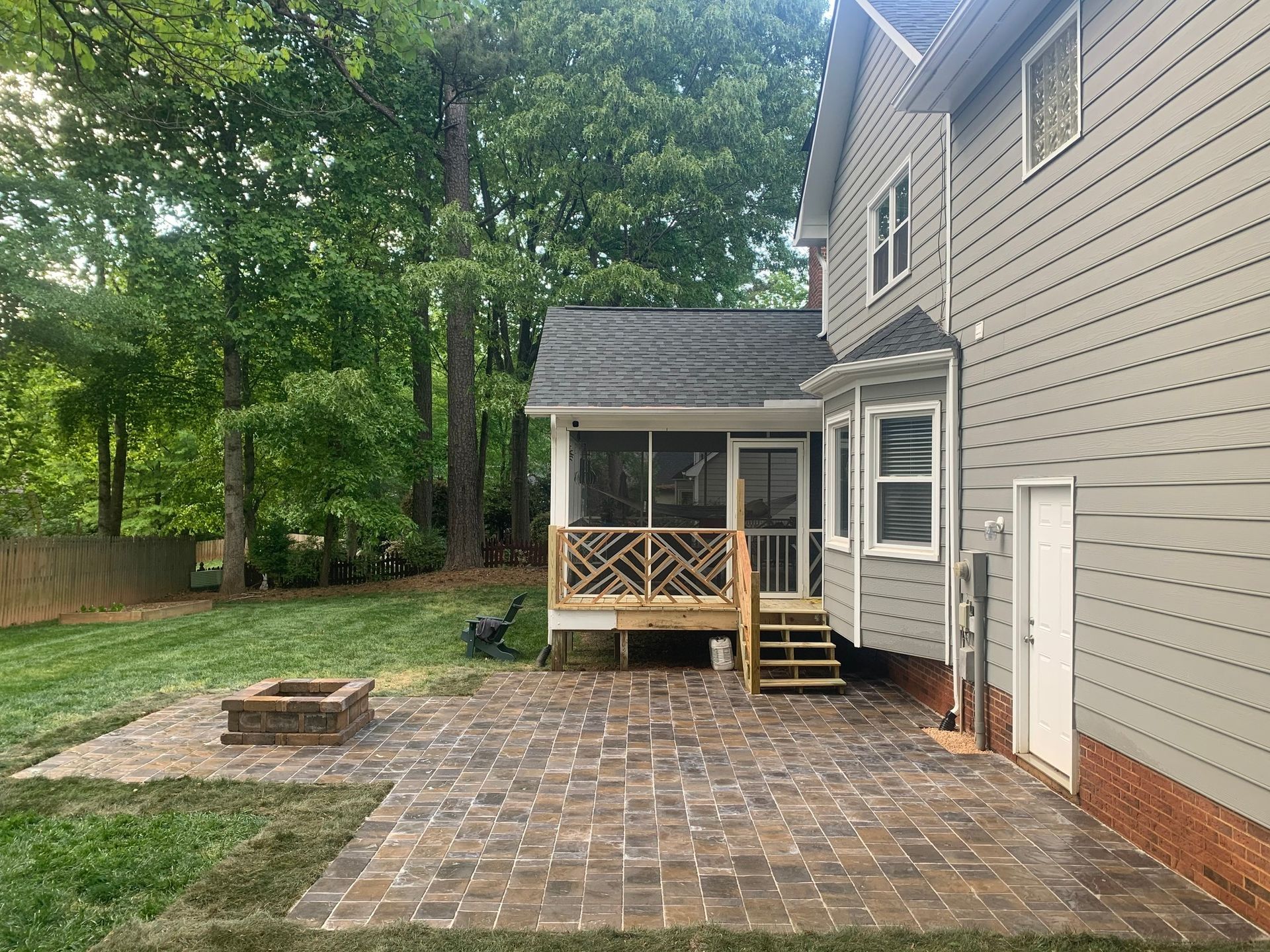 Patio with stone pavers, fire pit, screened porch, and gray house with green lawn.