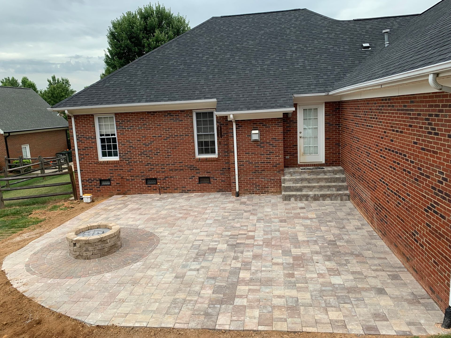 Brick patio with fire pit next to a red brick house.