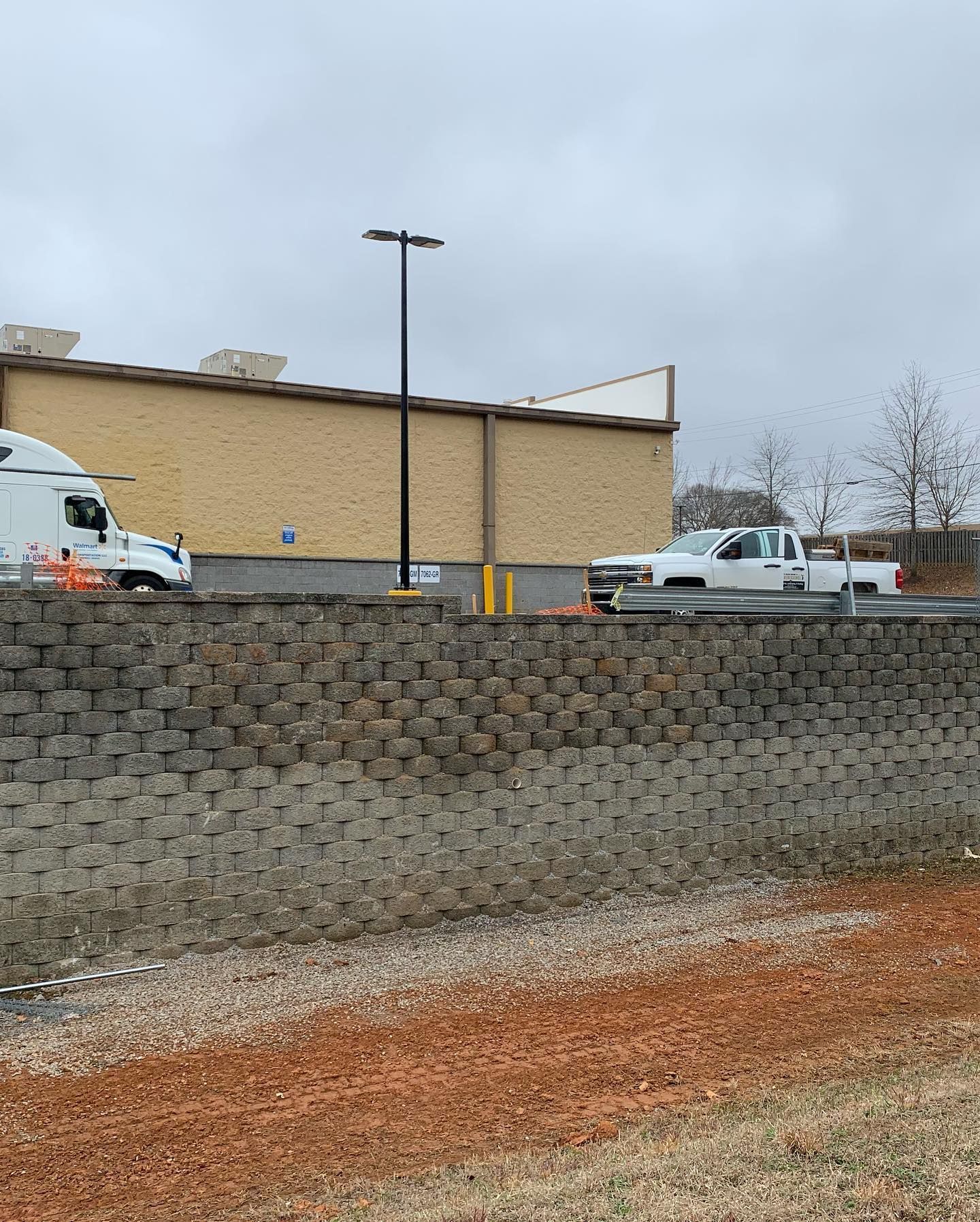 Brick retaining wall with a truck and a building in the background on an overcast day.
