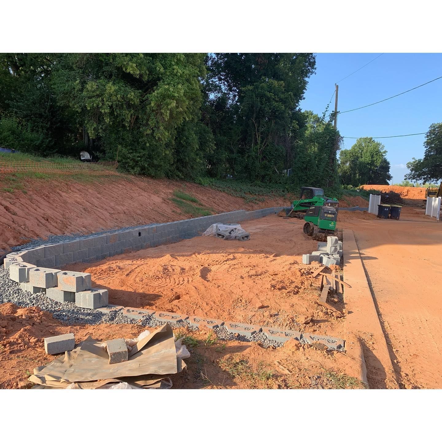 Construction of a retaining wall. Blocks and equipment on a dirt site next to a road.