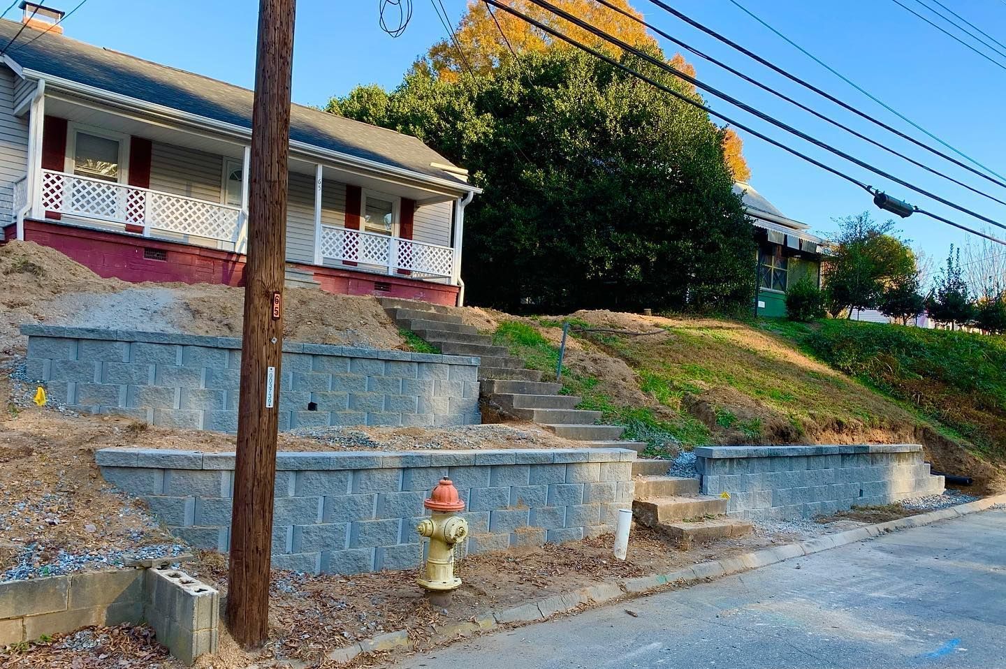A two-story house on a sloped lot with stone retaining walls, steps, and a fire hydrant.