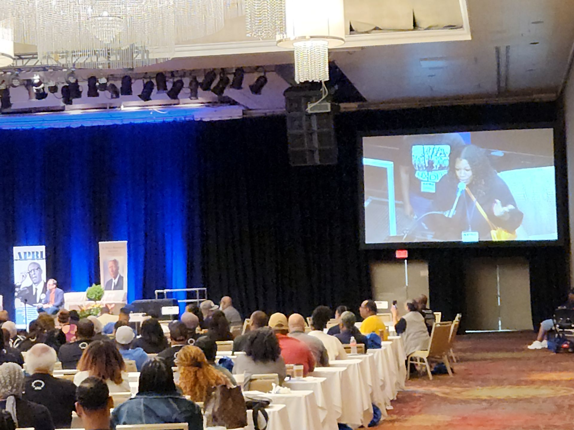 A group of people are sitting at tables in front of a screen that says APRI, at the APRI 52nd National Education Conference