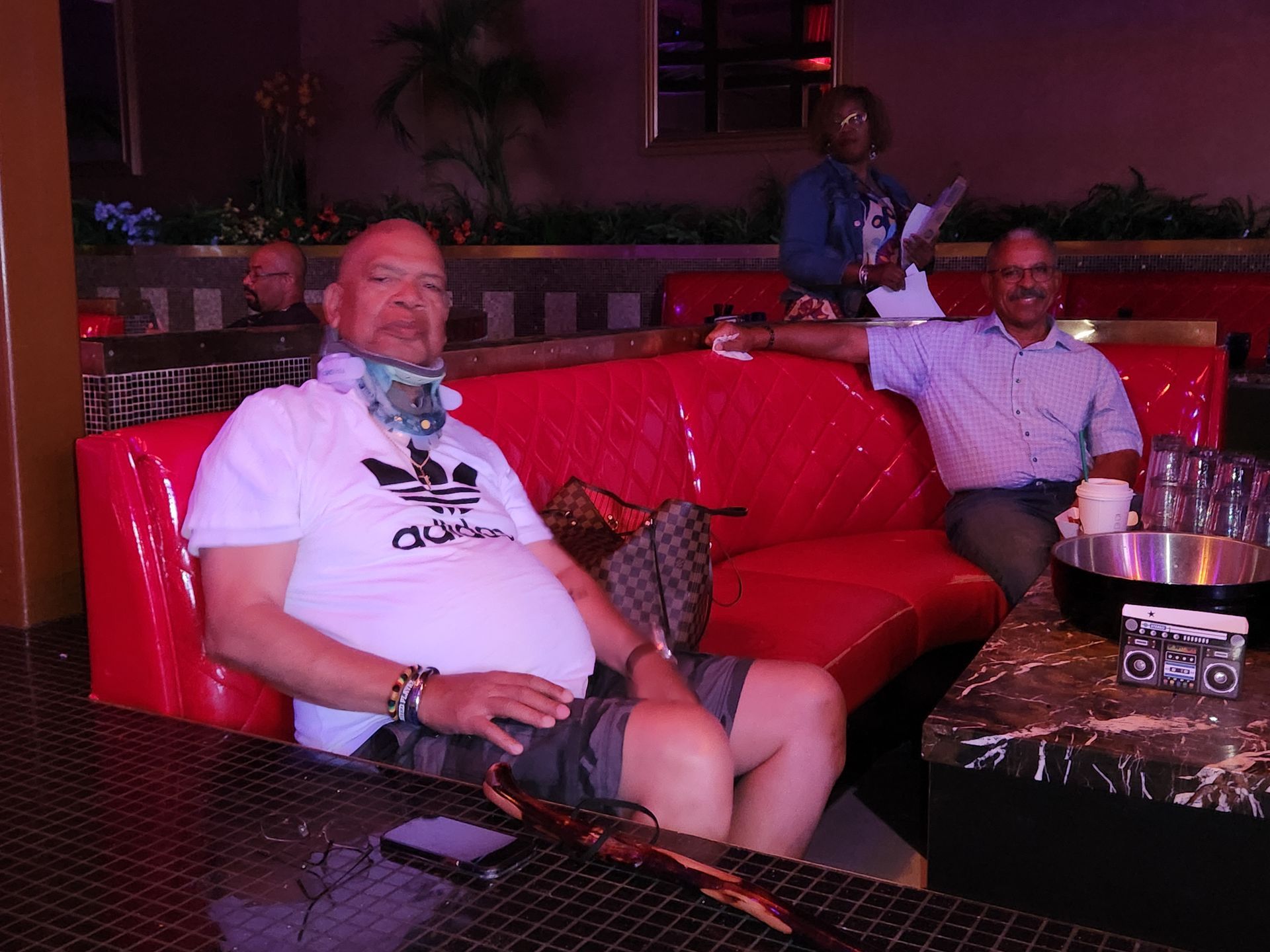 A man wearing a white adidas shirt is sitting on a red couch.