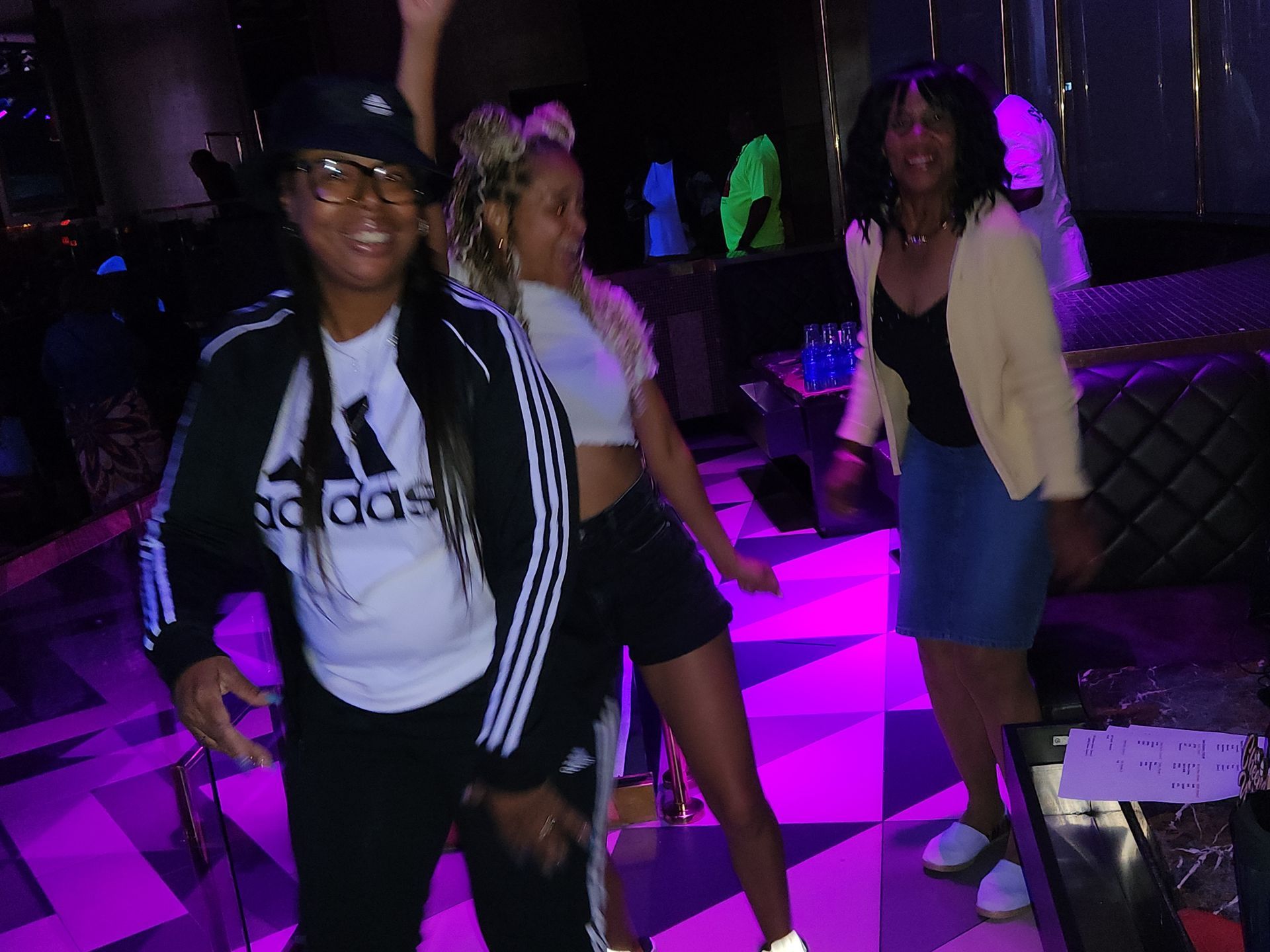 Women dancing with purple lights, one with an Adidas track suit,  at an APRI 