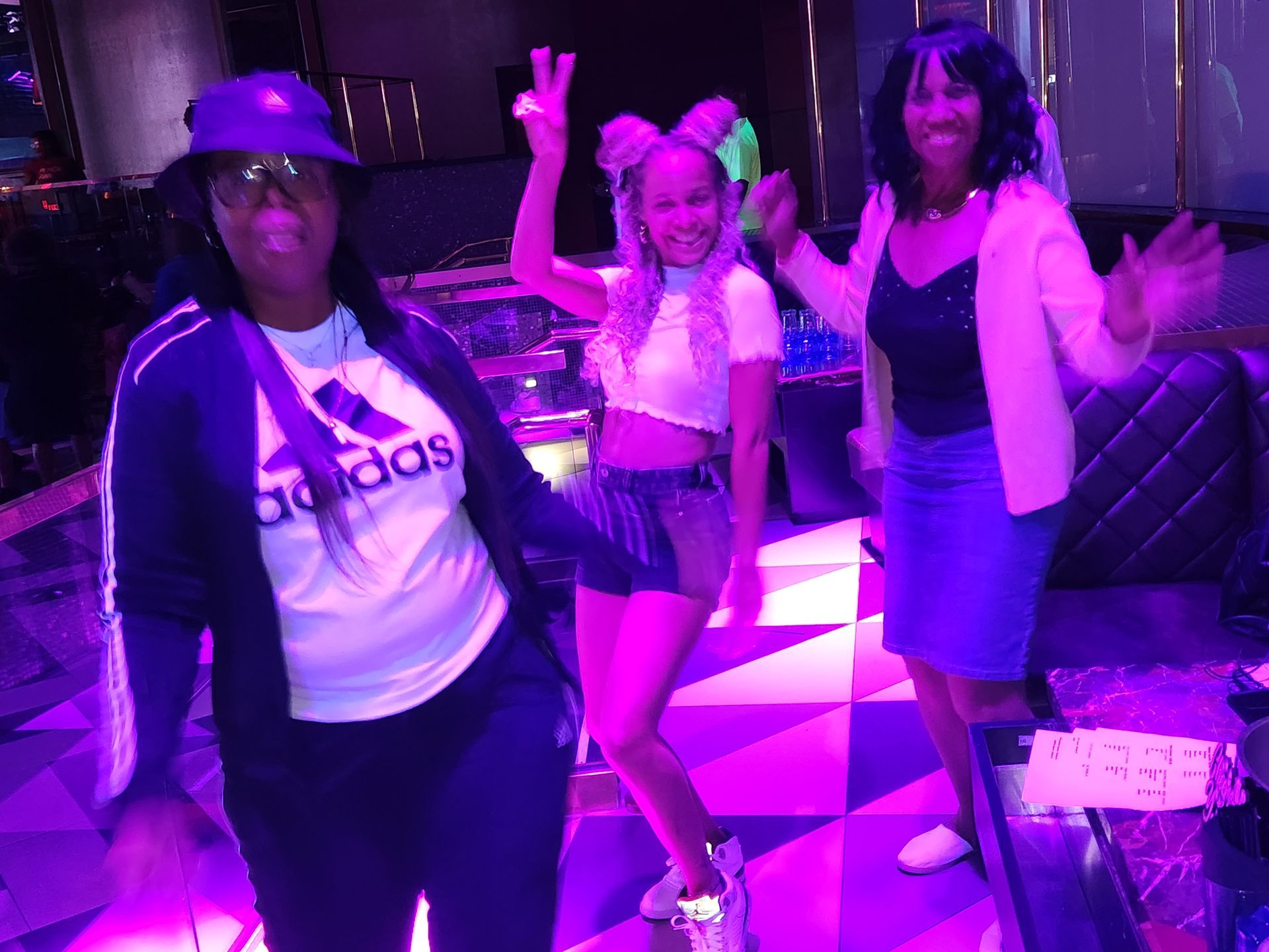 Three women are posing for a picture in a room with purple lights at an APRI 