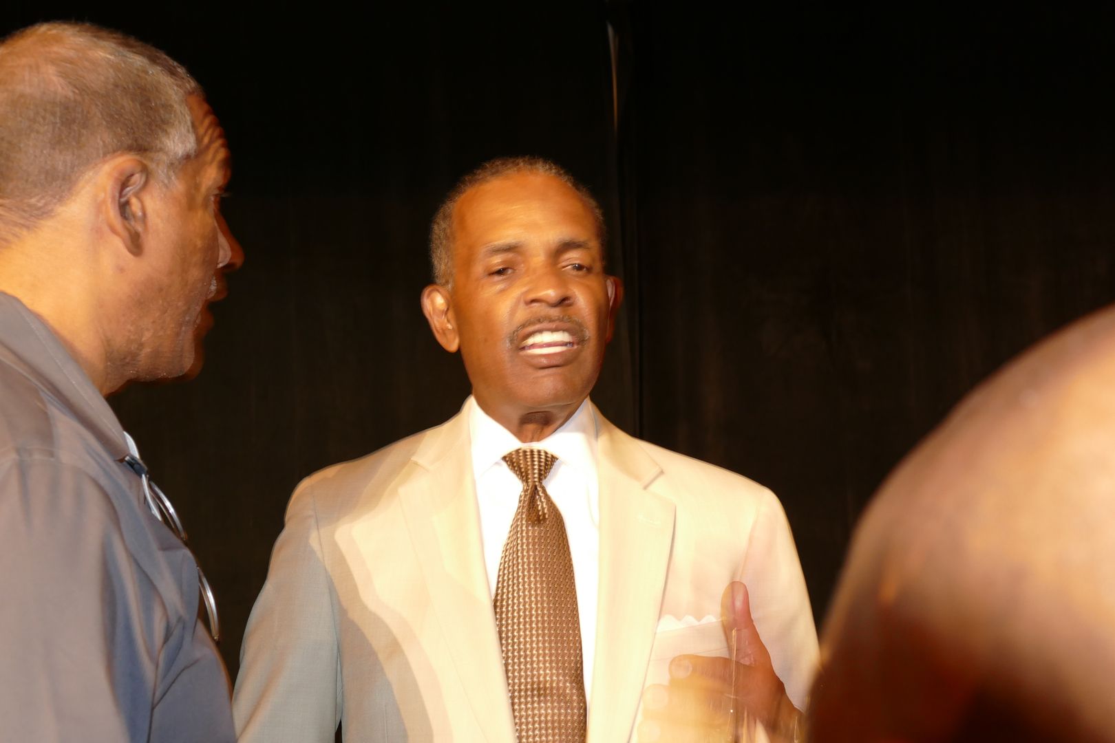 A man in a suit and tie is talking to another man  at an APRI event